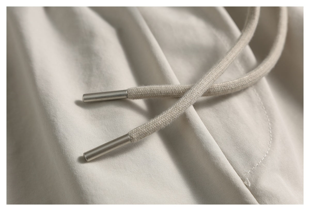 Close-up of two braided drawstring ends with metal tips on light beige shorts.