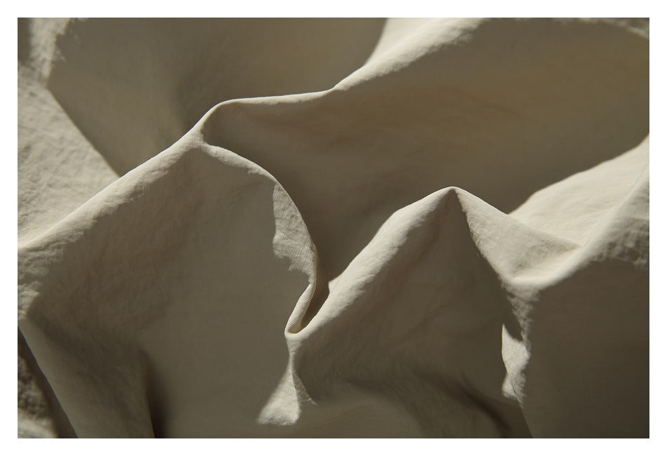 Close-up of softly folded beige fabric in warm natural light, showing its subtle woven texture.