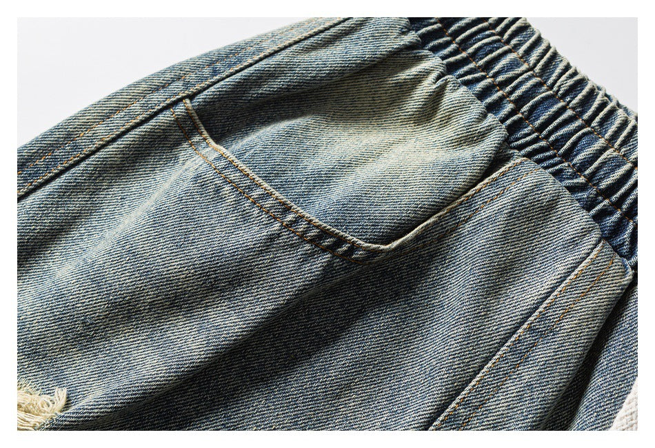 Close-up of a curved front pocket and elastic waistband on faded blue denim shorts.