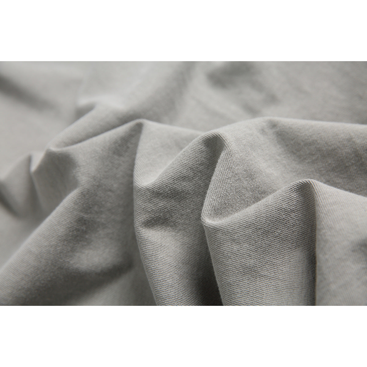 Close-up of gray T-shirt fabric arranged in soft folds, showing its surface and knit texture.
