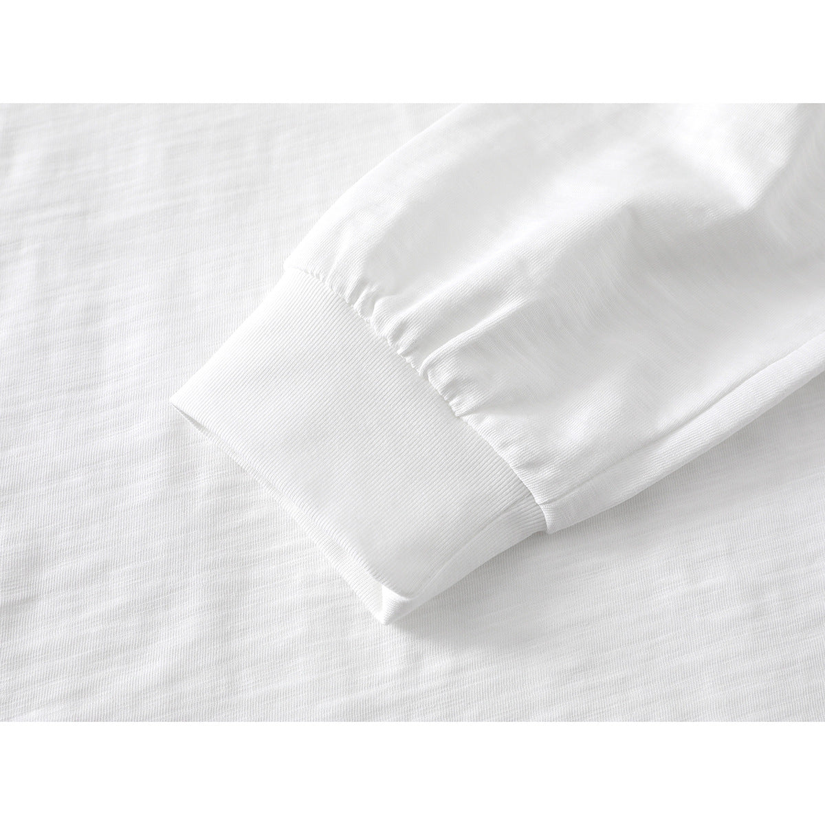 Close-up of a white long-sleeve shirt’s gathered sleeve and wide ribbed cuff.