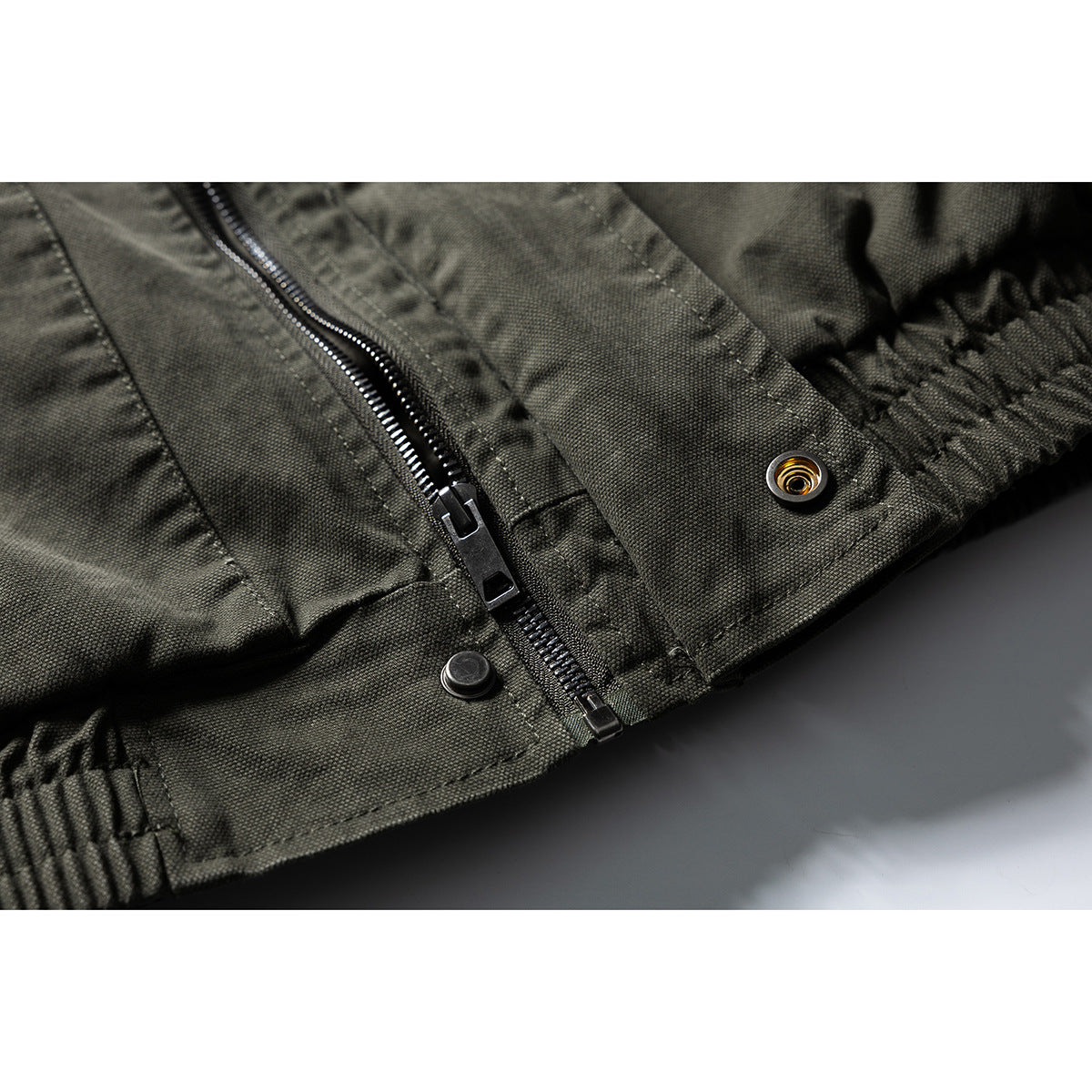 Close-up of an olive drab jacket’s front zipper, snap fasteners and gathered hem.