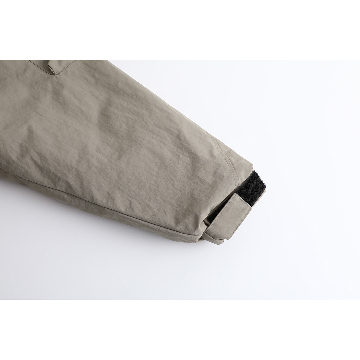 Close-up of a taupe jacket sleeve cuff with a black hook-and-loop adjustment tab.