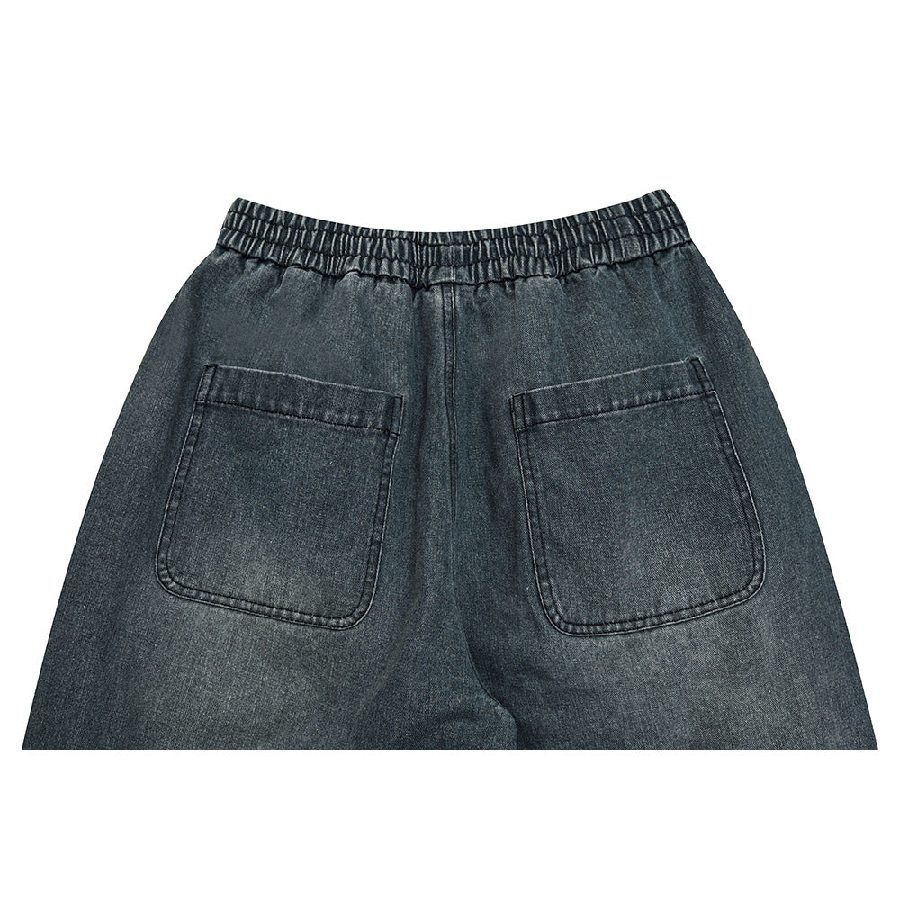 Upper back view of dark gray denim pants with an elastic waistband and two patch pockets.