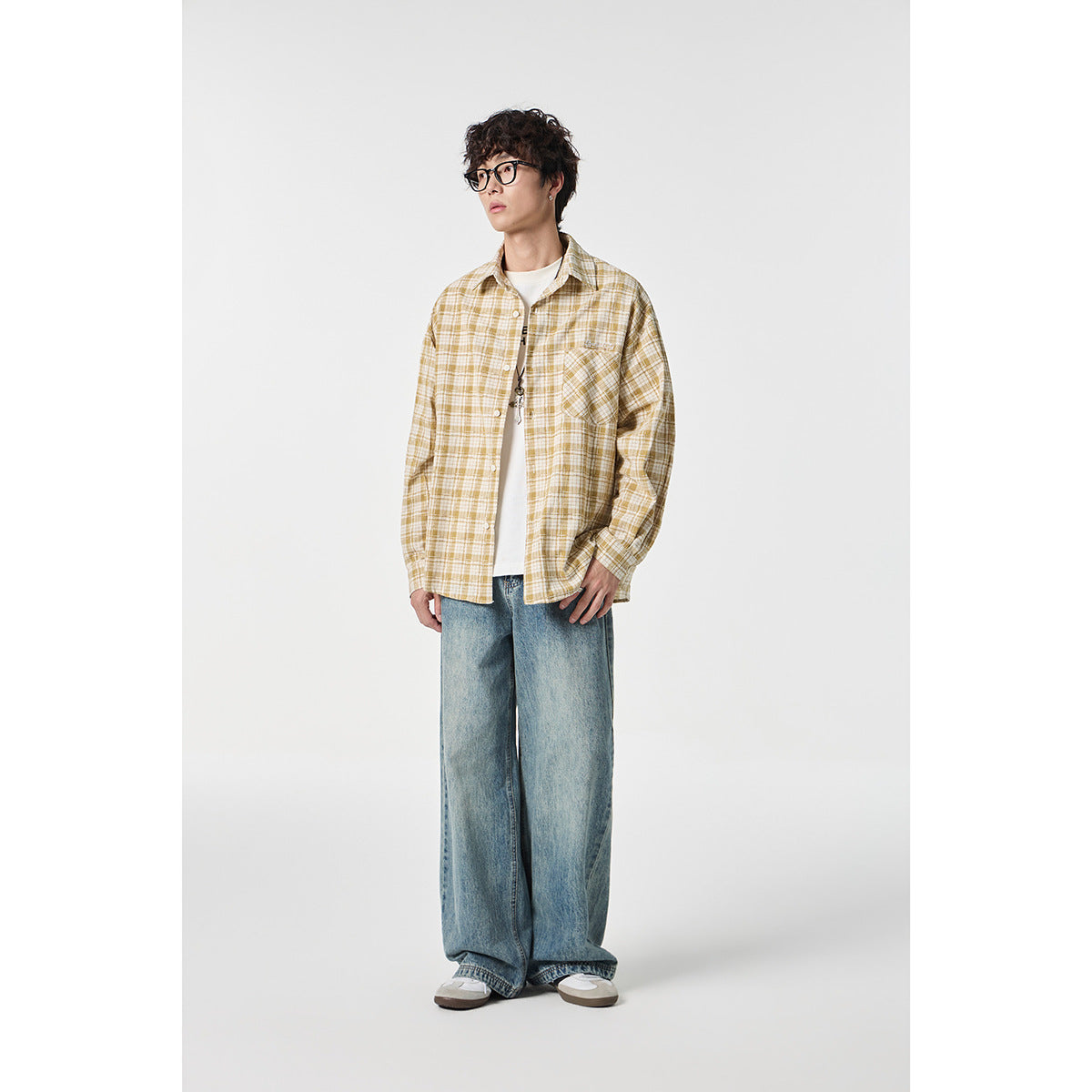 Model wearing a mustard-and-cream plaid button-up shirt over a white tee, with loose blue jeans.