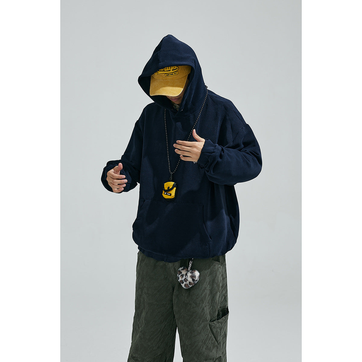 Model wearing an oversized navy pullover hoodie with a raised hood, chest pocket, and small embroidered design.