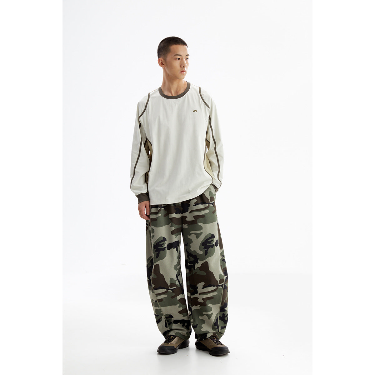 Model wearing a cream long-sleeve top with dark piping and loose green camouflage pants.