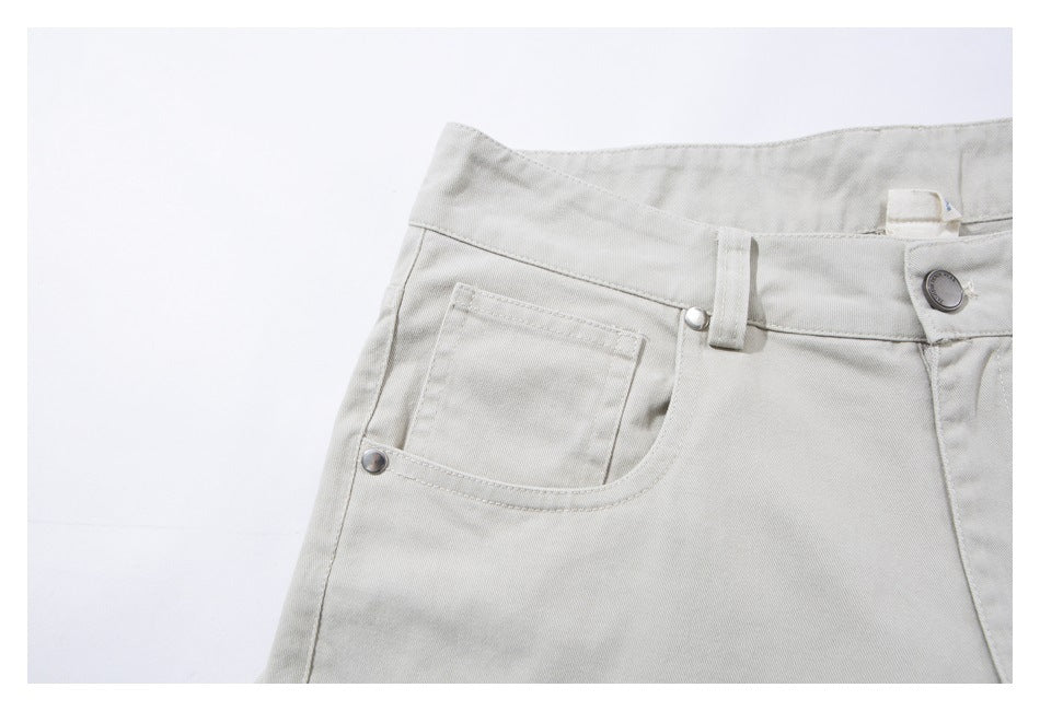 Close-up of light beige trousers showing the front waistband, button, belt loop and riveted pocket.