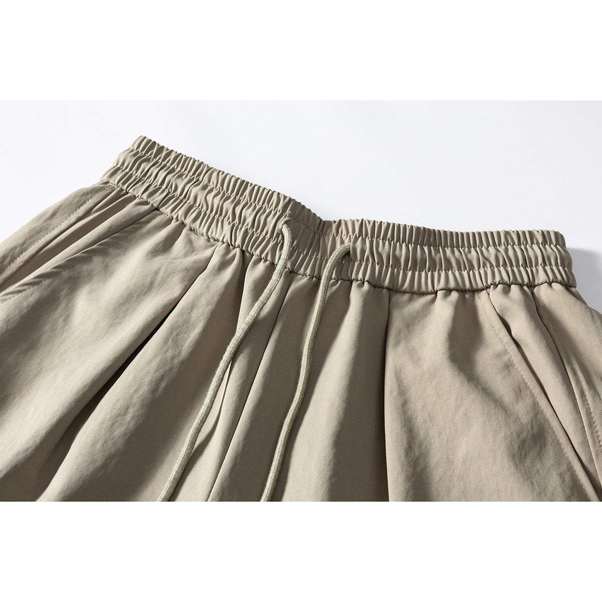 Close-up of beige pants showing the gathered elastic waistband, drawstring, and front pleats.