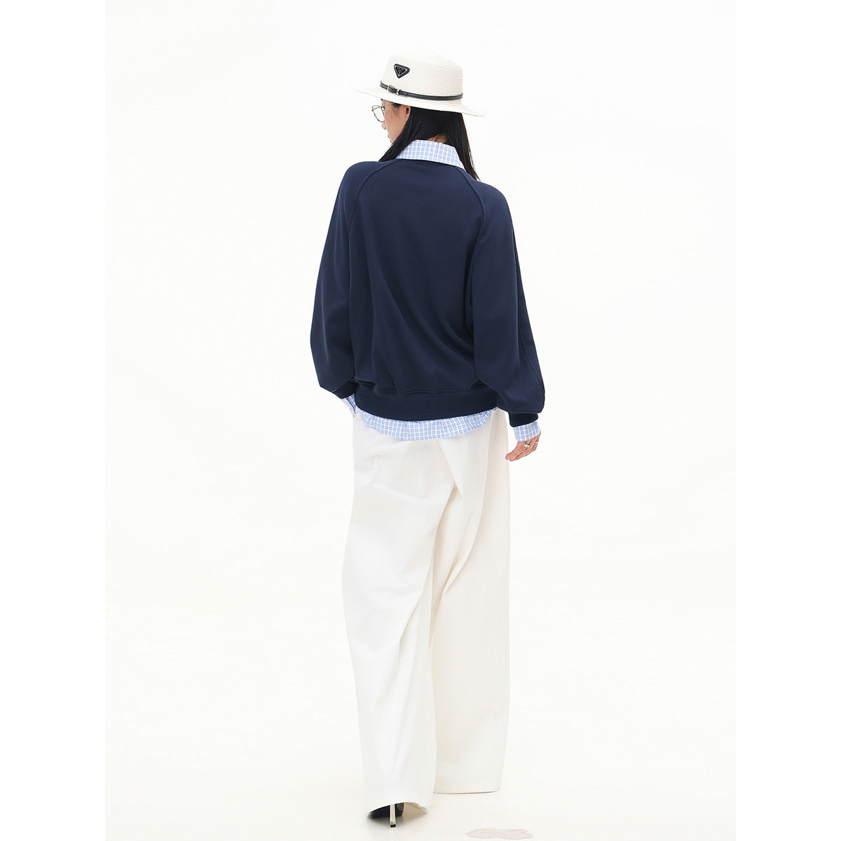 Back view of a model wearing a navy sweatshirt over a blue checked shirt with wide white trousers.