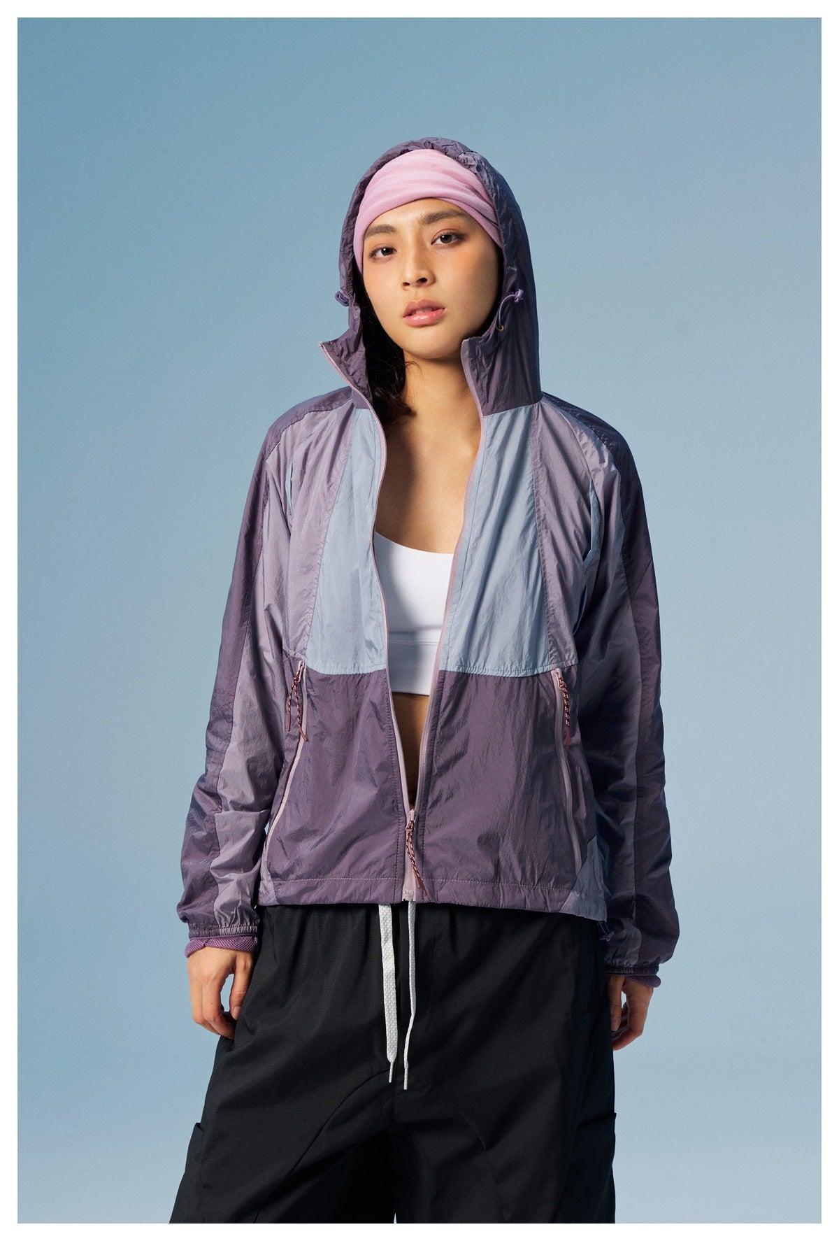 Model wearing an open purple and pale blue color-block hooded jacket over a white top, with black pants.