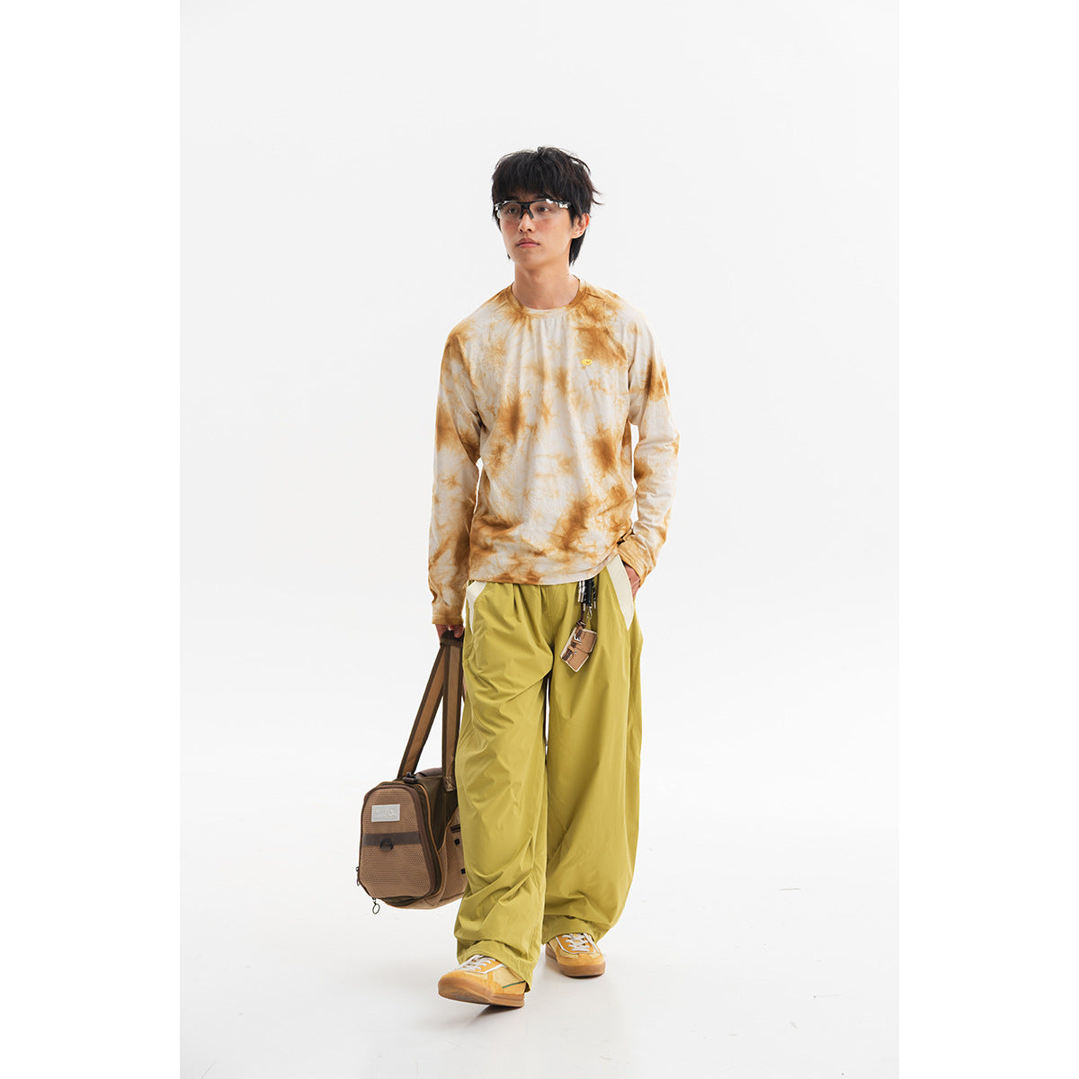 Model wearing a cream and ochre tie-dye long-sleeve crewneck shirt with loose yellow-green trousers.