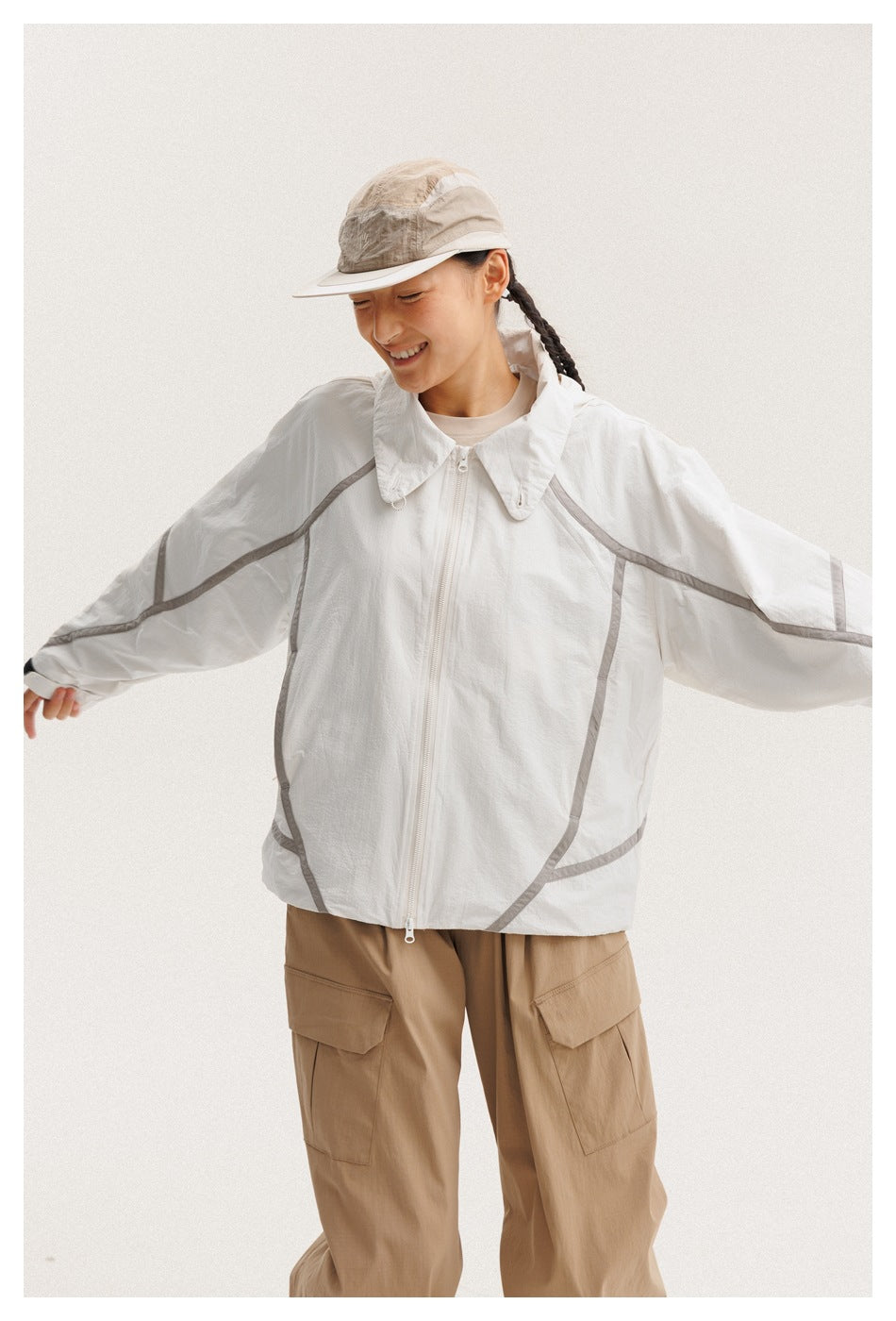 Model wearing a white zip-front jacket with gray piping and tan cargo pants, arms out to show the jacket.