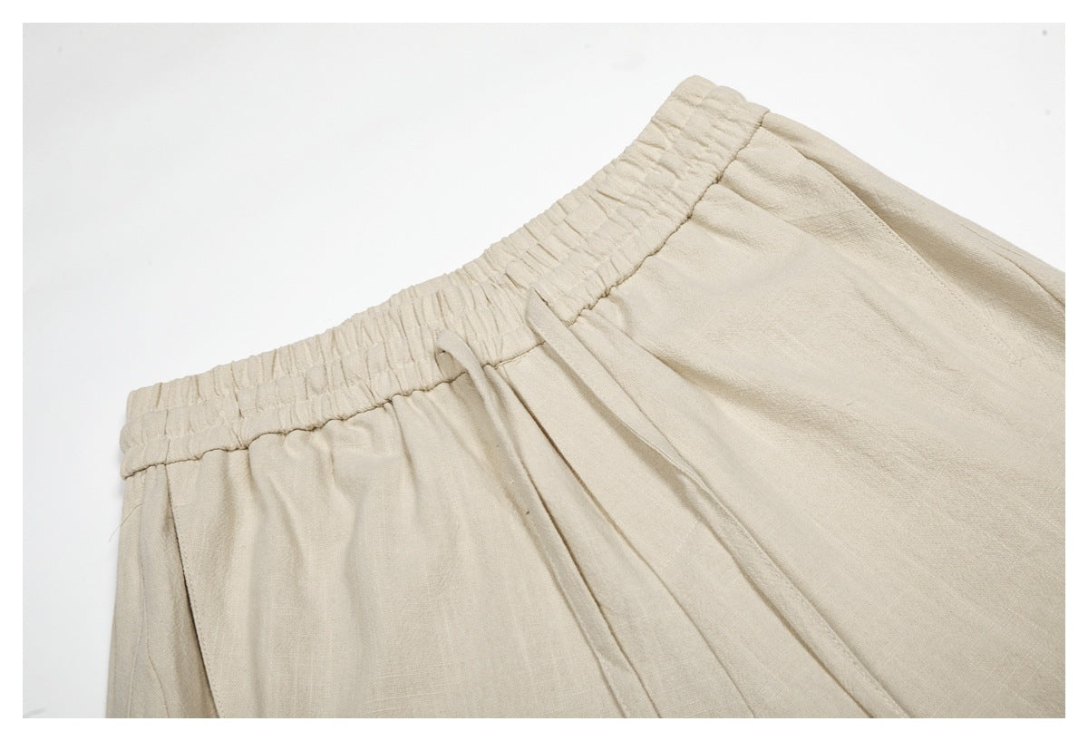 Close-up of beige trousers showing the gathered elastic waistband, drawstring, and front seam.