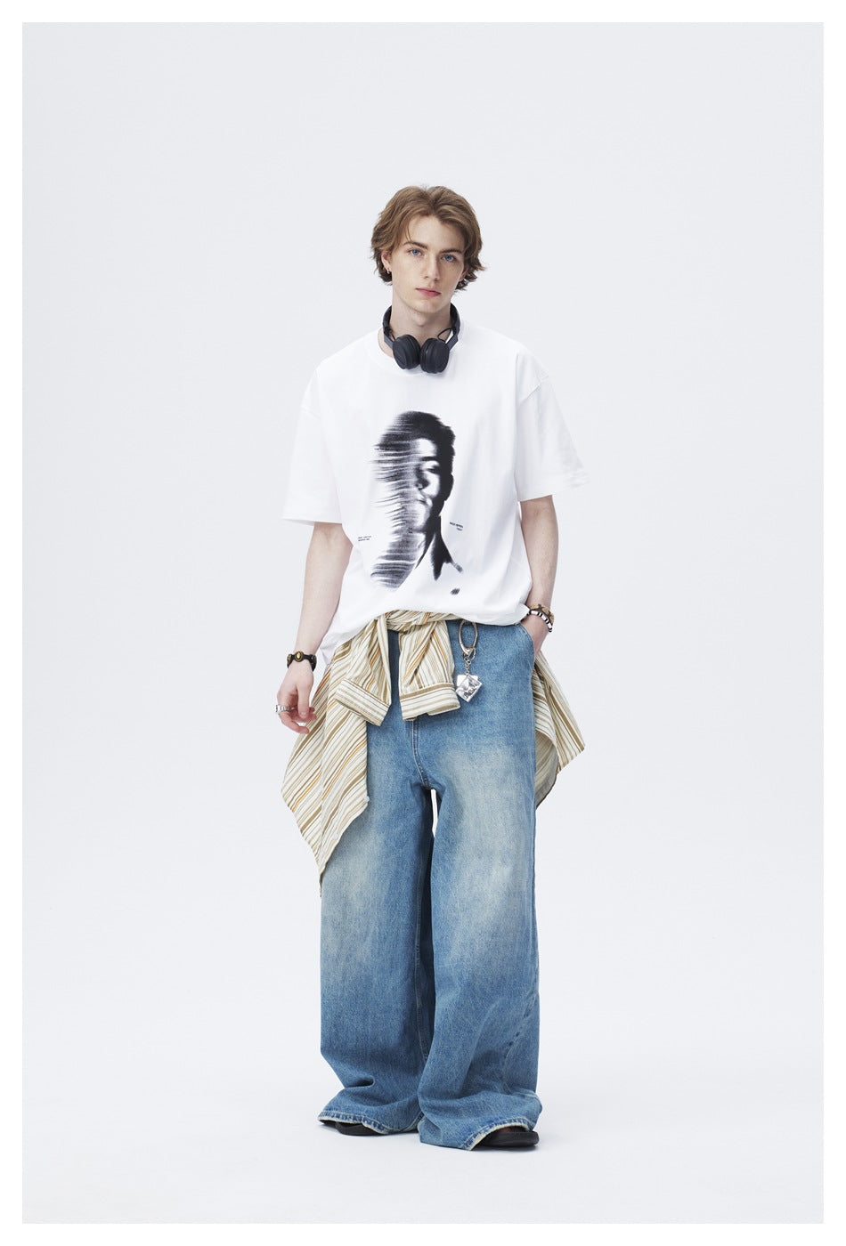 Model wearing a white graphic T-shirt with wide-leg blue jeans, a striped shirt tied at the waist and headphones