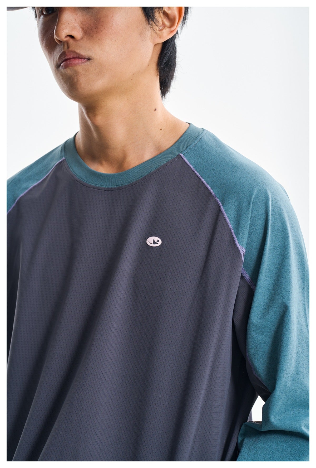 Close-up of the shirt’s charcoal perforated front panel, teal raglan sleeve, lavender piping, and small chest emblem.