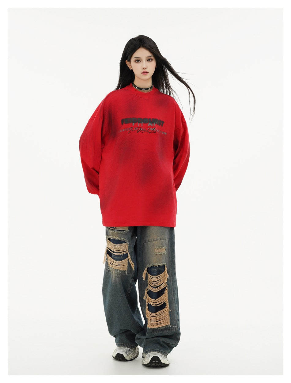 Full-length model wearing an oversized red long-sleeve shirt with chest lettering and distressed wide-leg jeans.