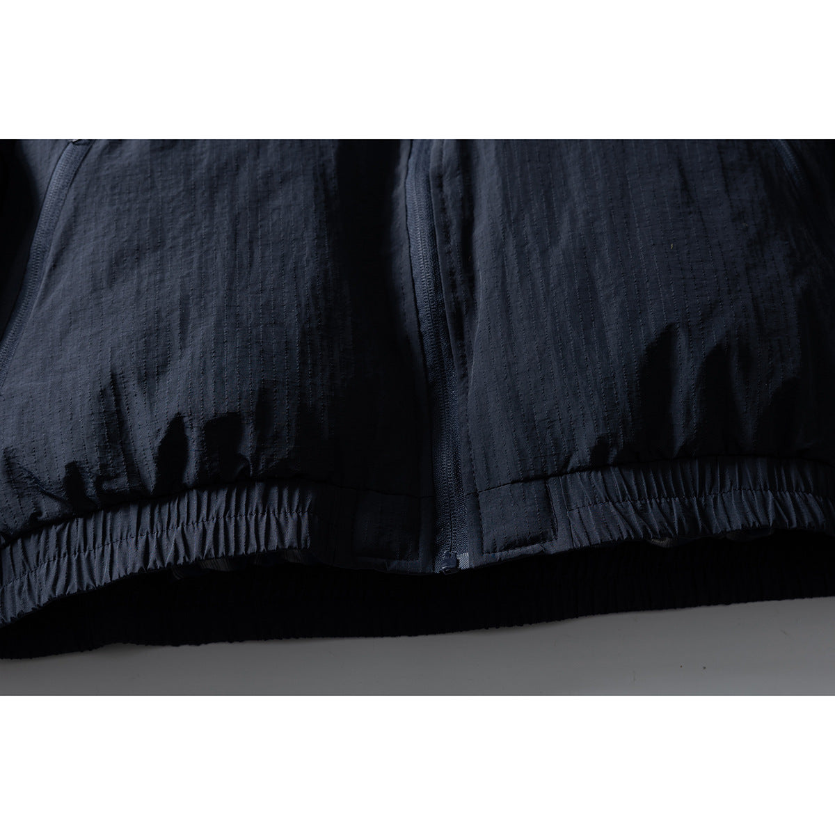 Close-up of the dark jacket’s front zipper, textured fabric, and gathered hem.