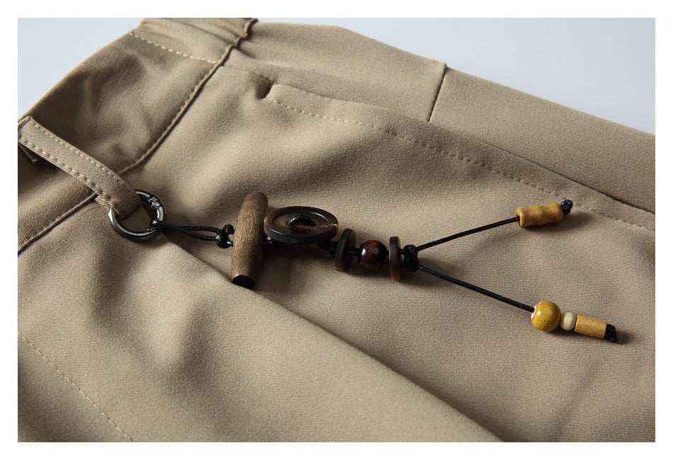Close-up of a decorative beaded cord attached to a belt loop on beige trousers.