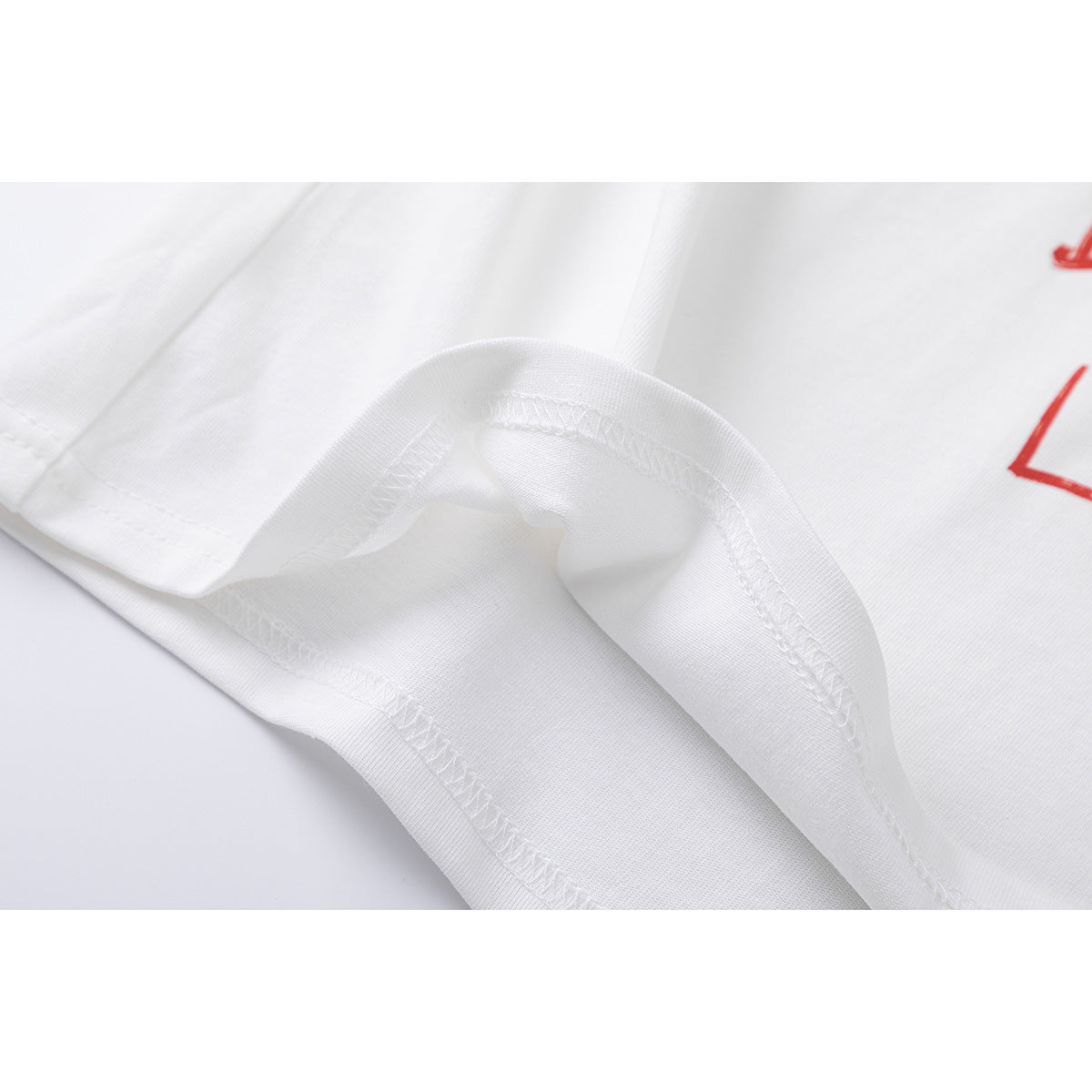 Close-up of the white T-shirt's hem and overlock stitching, with a small portion of red print visible.