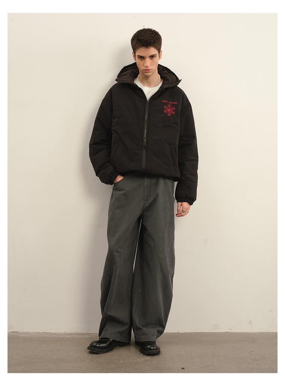 Front view of a model wearing a black hooded zip jacket with red chest embroidery and wide-leg gray jeans.