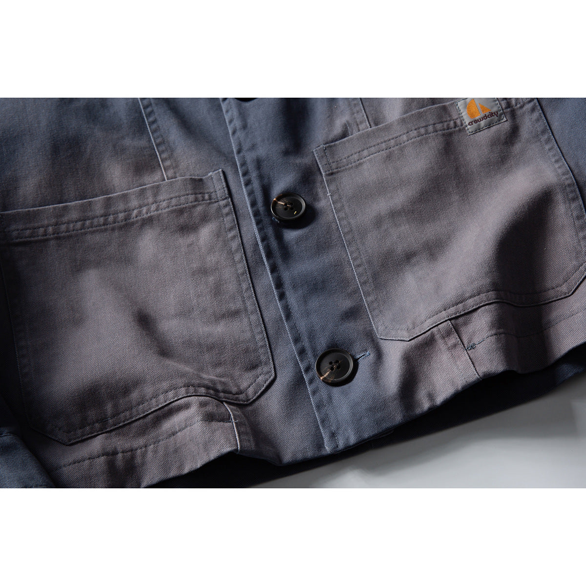 Close-up of a gray jacket front with two patch pockets, dark buttons, and a small logo patch.