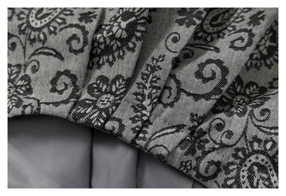 Close-up of gray fabric with a black floral and paisley pattern, showing folded stitched edges.