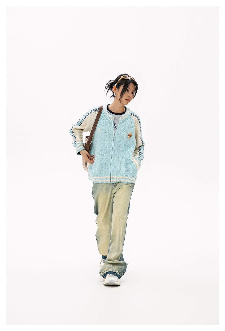 Full-length model wearing a pale blue and cream patterned cardigan with loose faded jeans and sneakers.