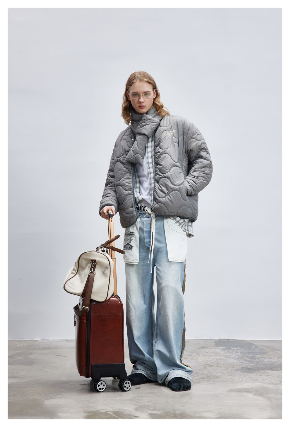 Model wearing a gray wave-quilted jacket with a matching scarf, plaid shirt, and loose light-blue jeans.