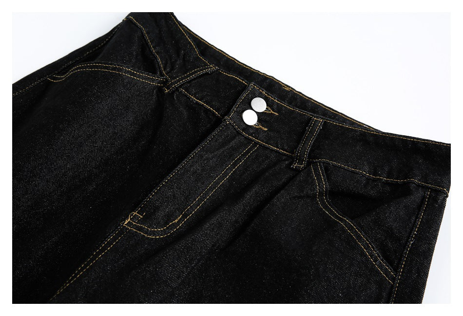 Close-up of black jeans with gold topstitching, belt loops, front pocket and two silver waist buttons.