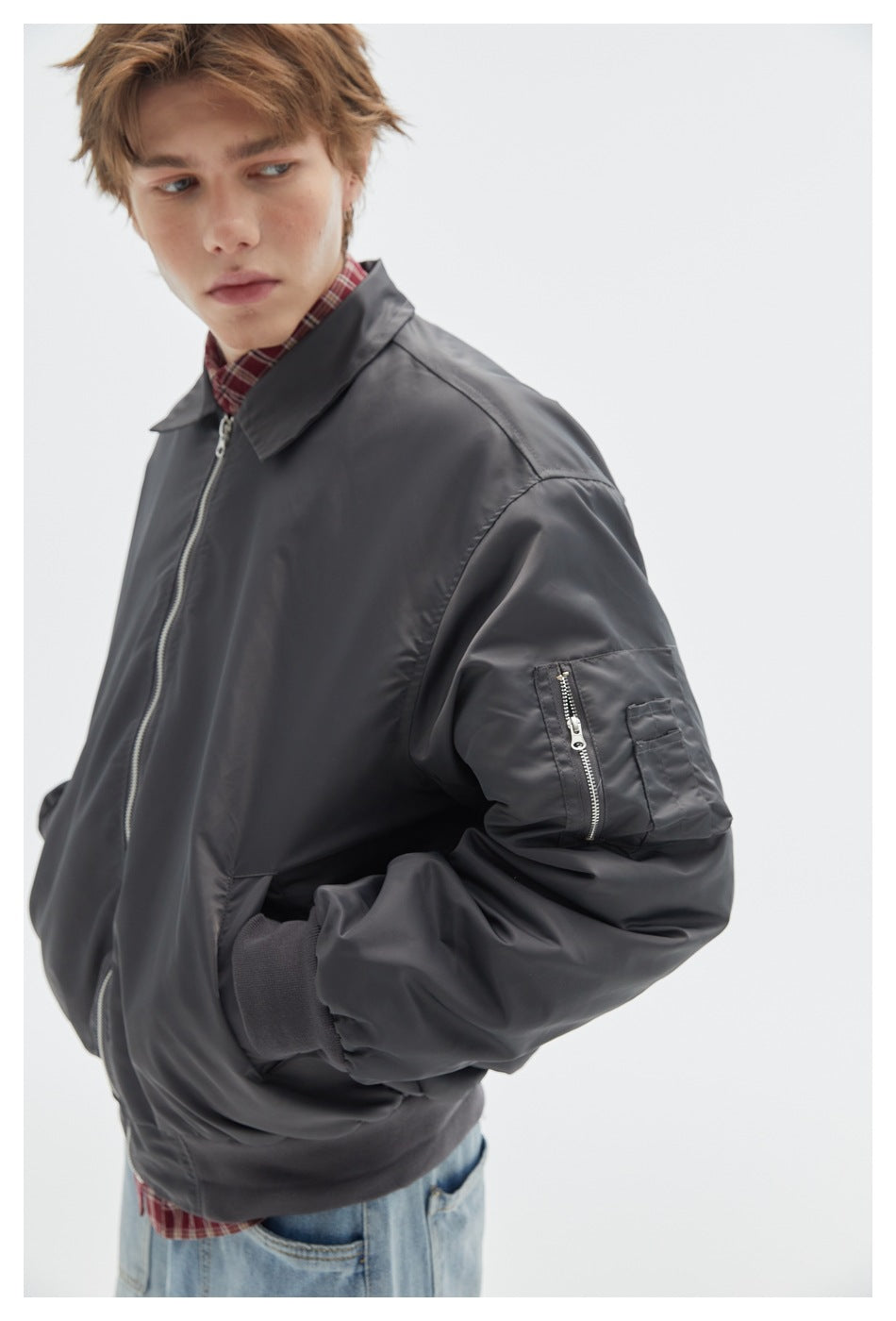 Close view of a model wearing a charcoal gray jacket, showing its zip front, pointed collar, and zippered sleeve pocket.