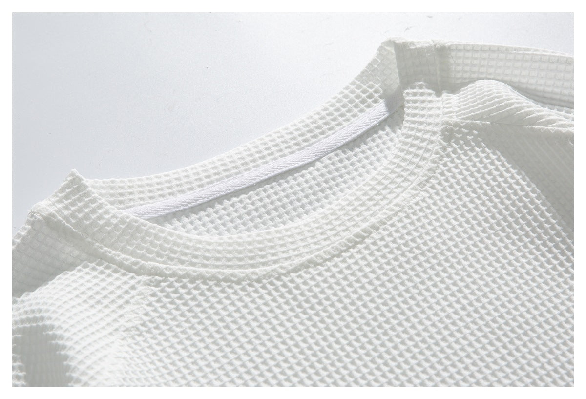 Close-up of a white waffle-textured garment showing its rounded neckline and stitched edge.
