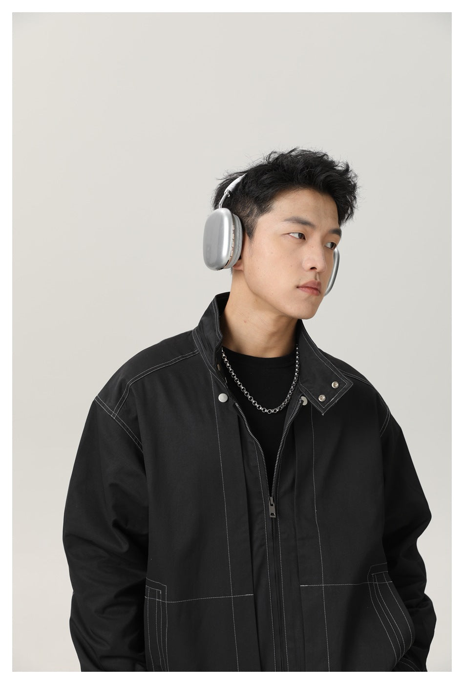 Model wearing a black jacket with contrast stitching, a stand collar, silver snaps and a front zipper.