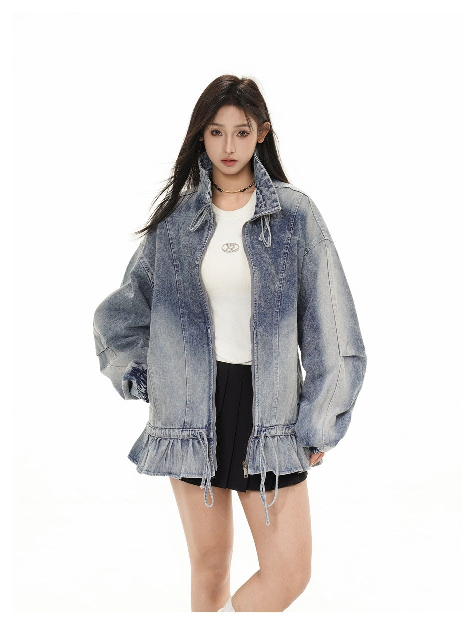 Closer front view of a model in a washed blue denim jacket with a tall collar, front zipper and drawstring hem.