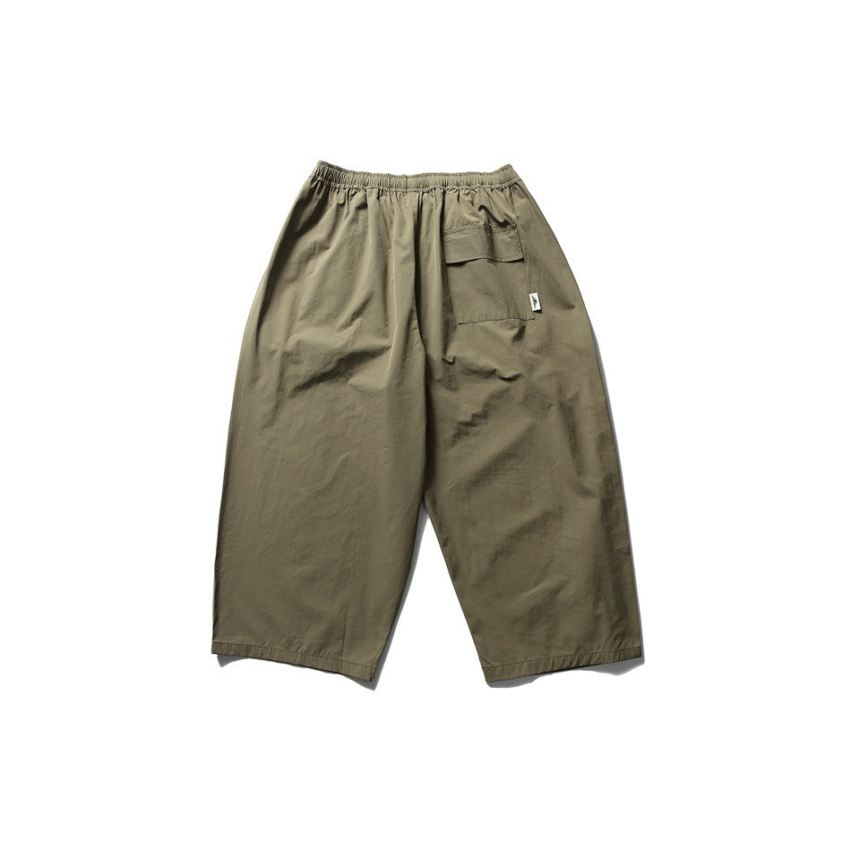 Rear view of loose olive pants with an elastic waistband and a flap cargo pocket.