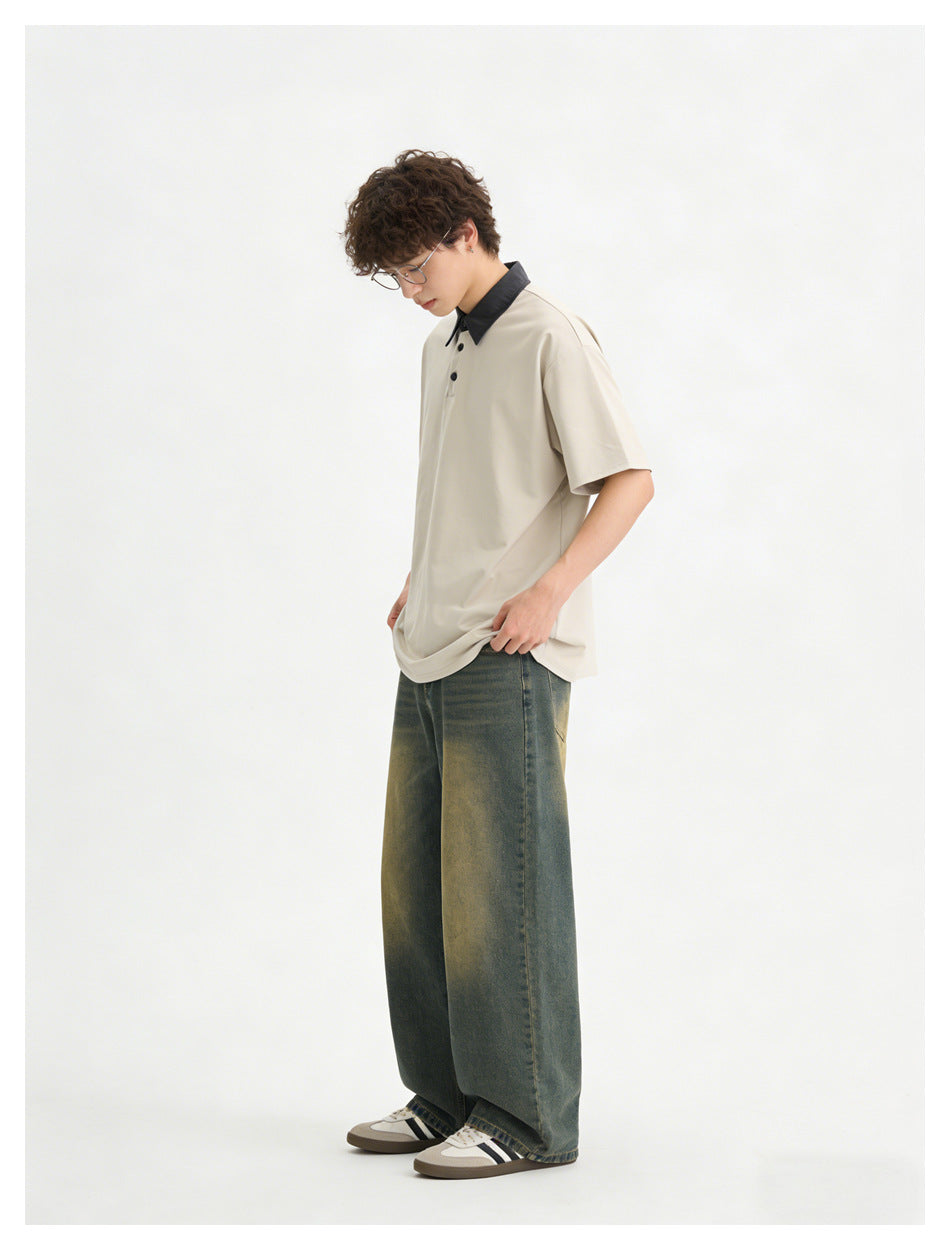 Model wearing a light beige short-sleeve polo with a black collar and loose, faded dark jeans.