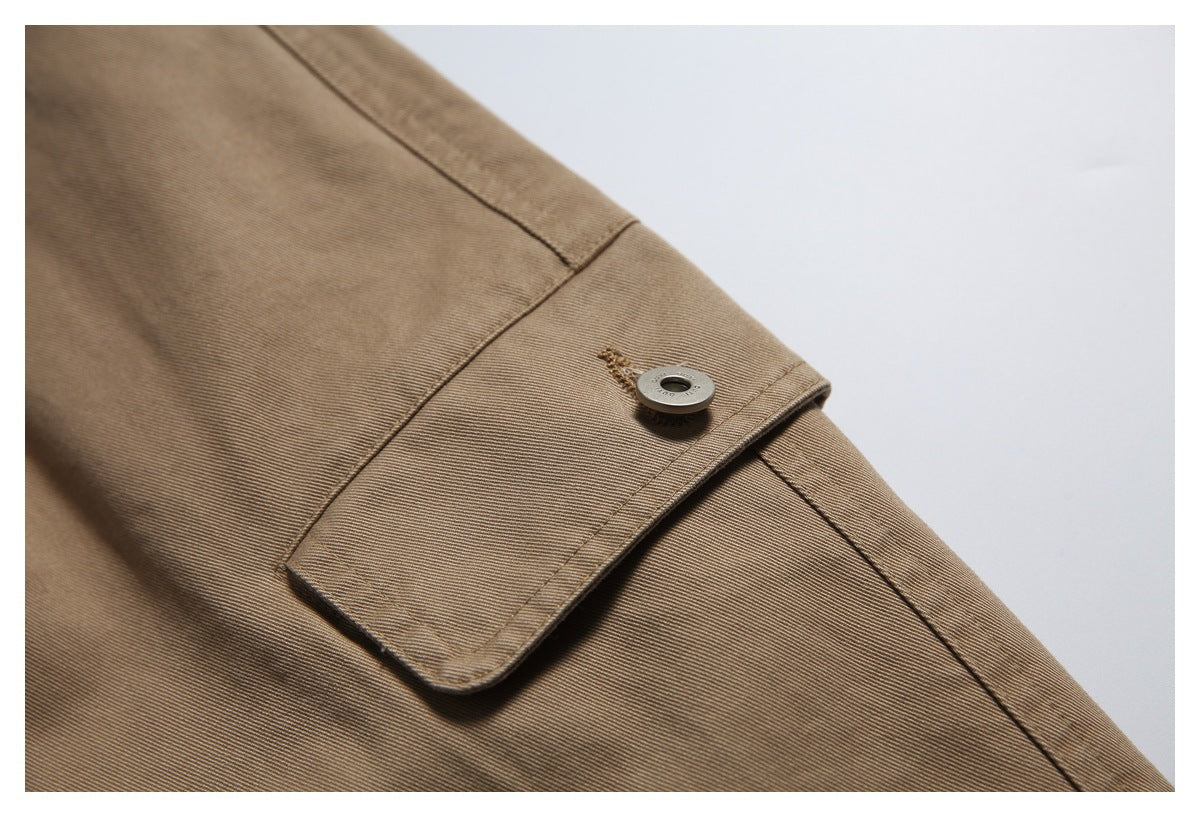 Close-up of a buttoned tab and seam on tan trousers.