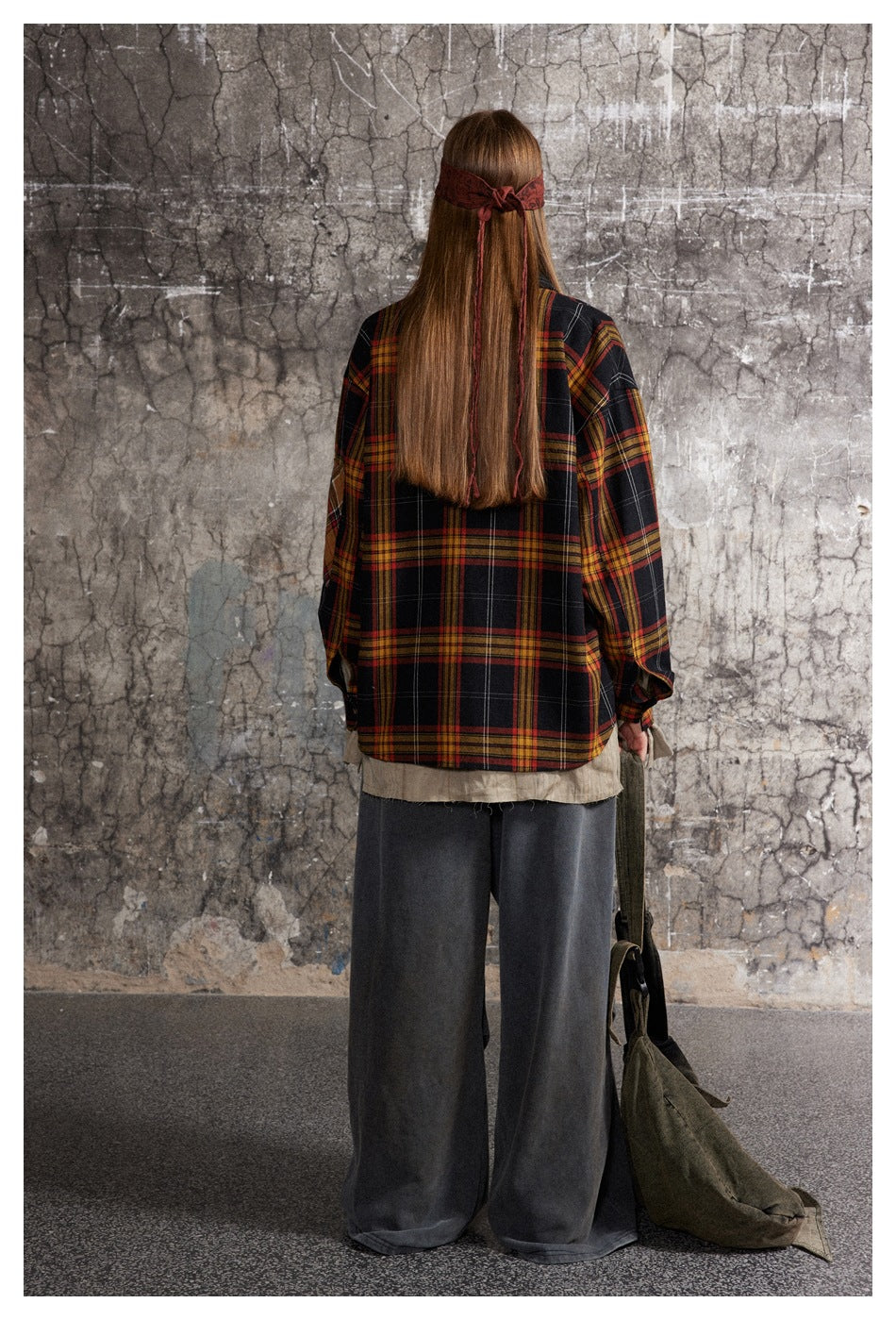 Back view of a model wearing an oversized black plaid shirt-jacket with red and mustard stripes.