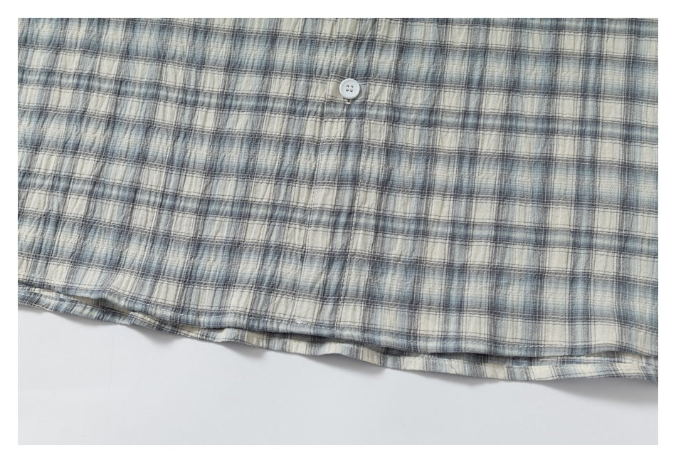 Close view of the hem and a white button on a gray, blue, and cream plaid shirt.