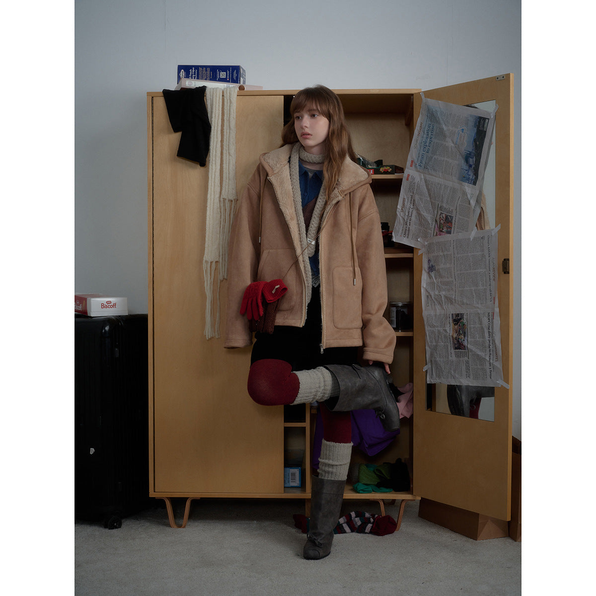 Model wearing a tan shearling-lined zip jacket, layered knitwear, a black skirt, burgundy tights and tall boots.