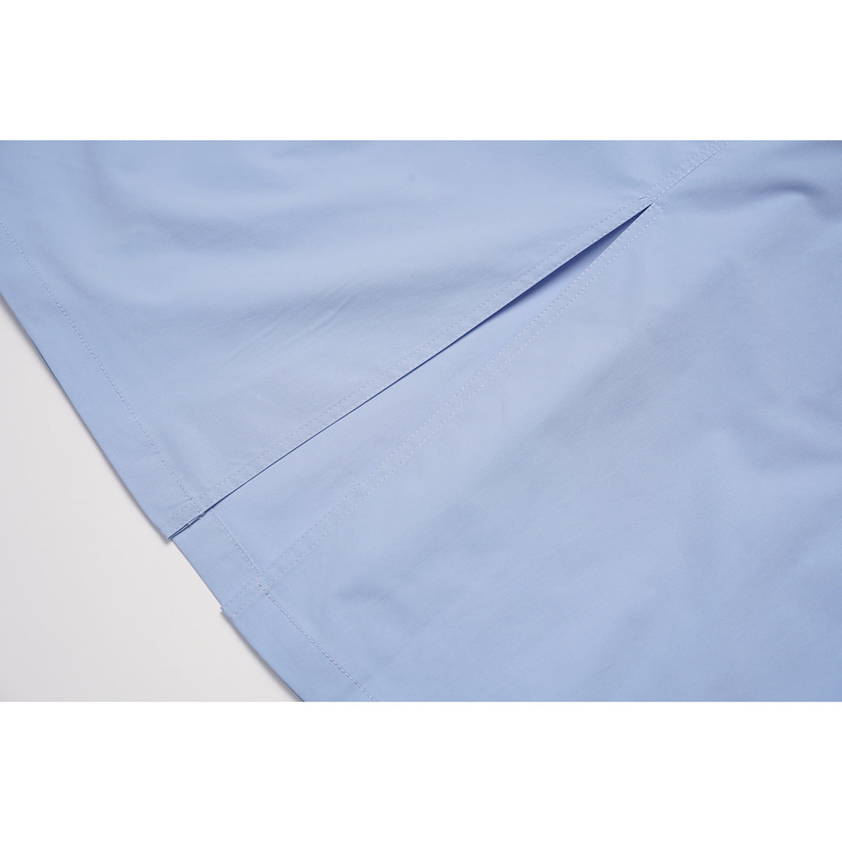 Close-up of a light blue skirt's stitched hem and side slit.