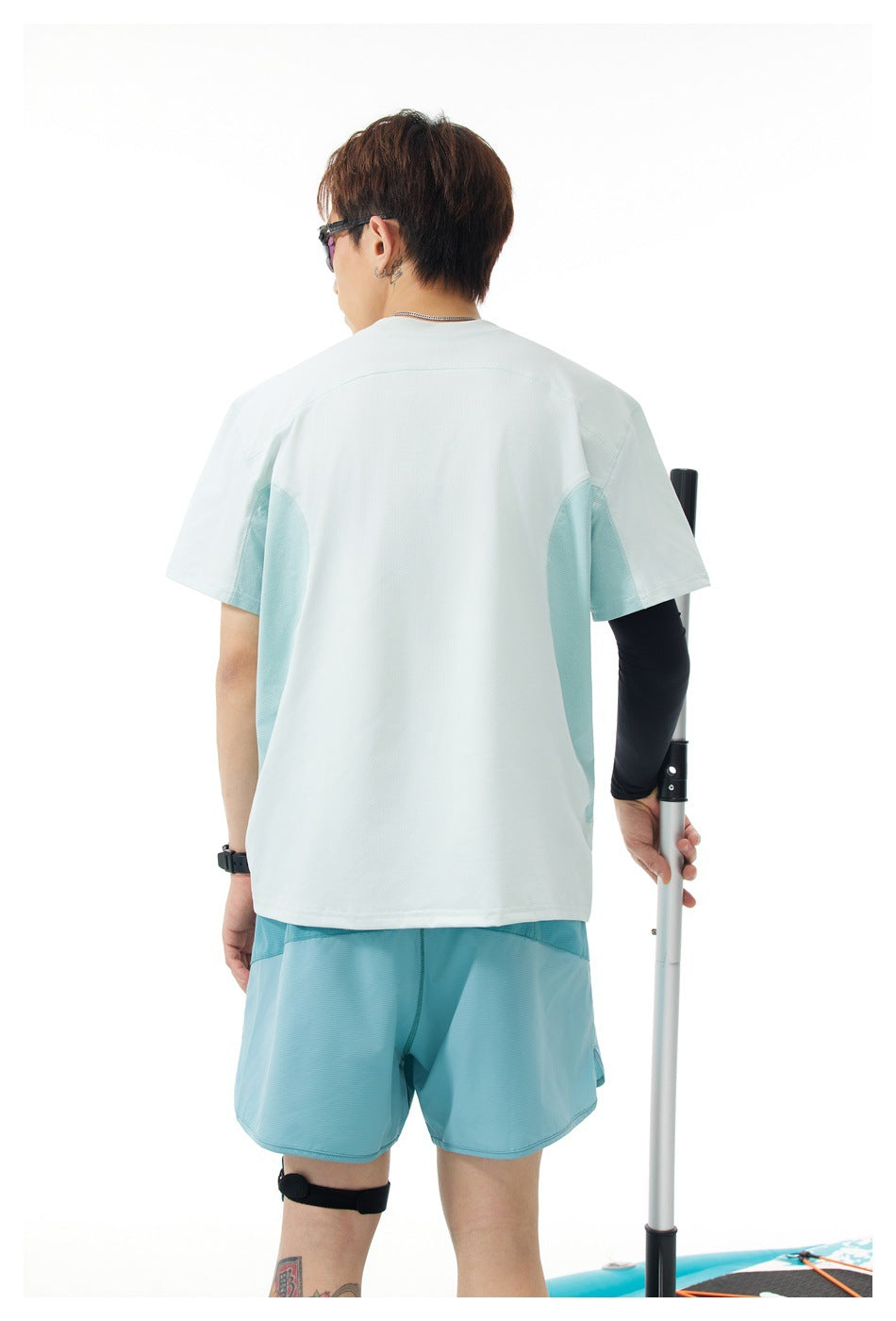 Back view of a man in a pale mint T-shirt with light teal side panels, wearing blue shorts