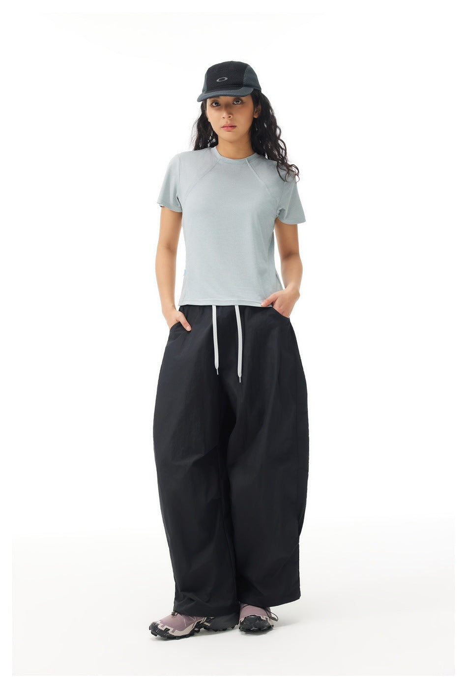 Model wearing a gray-green short-sleeve T-shirt with black wide-leg drawstring pants and a black cap