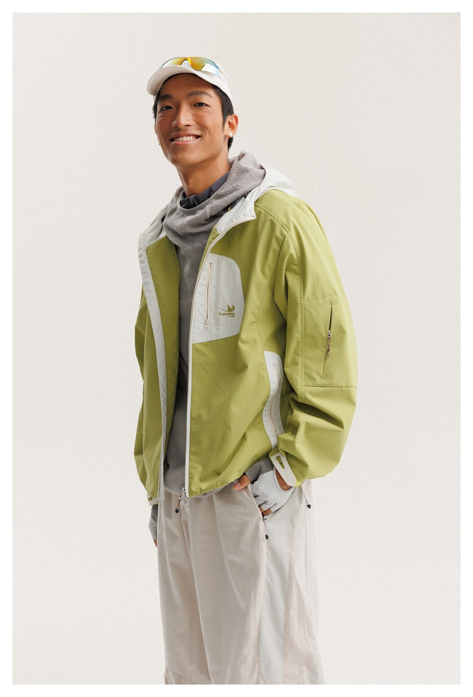 Man wearing a lime-green hooded jacket with white panels and a zip chest pocket, styled with light trousers.