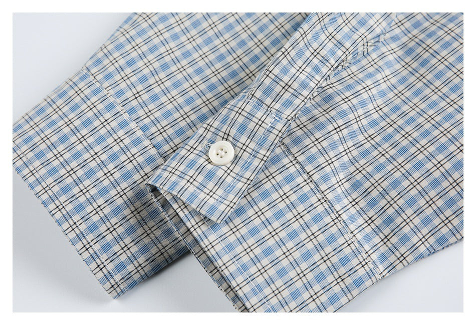 Close-up of a white-button cuff and stitching on a light blue, white, and black plaid shirt.