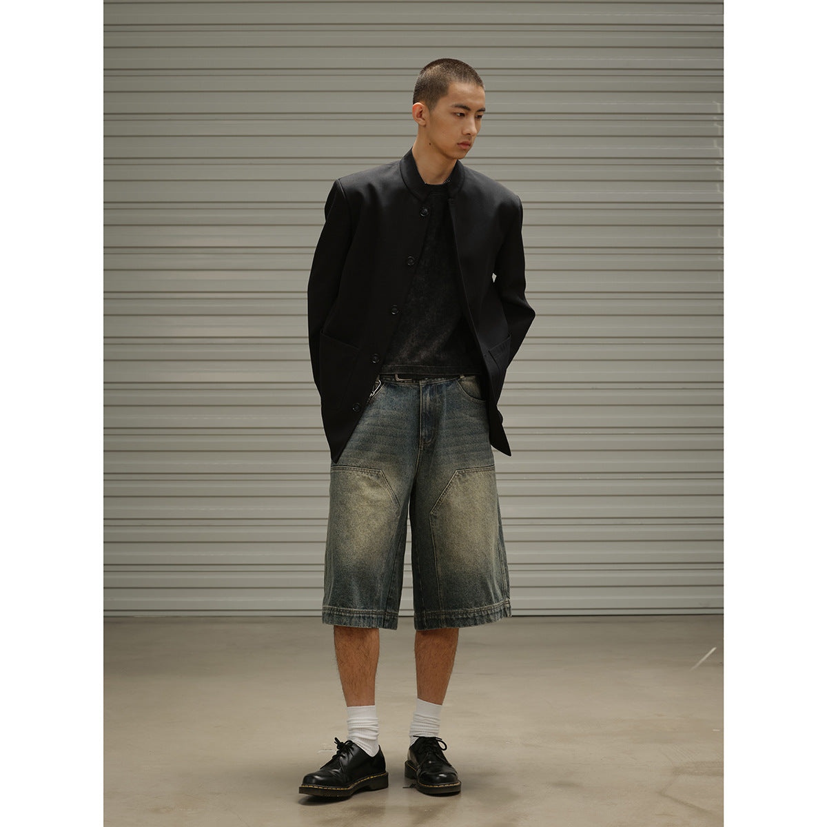 Model wearing a long black button-front coat over a black top and oversized faded denim shorts.