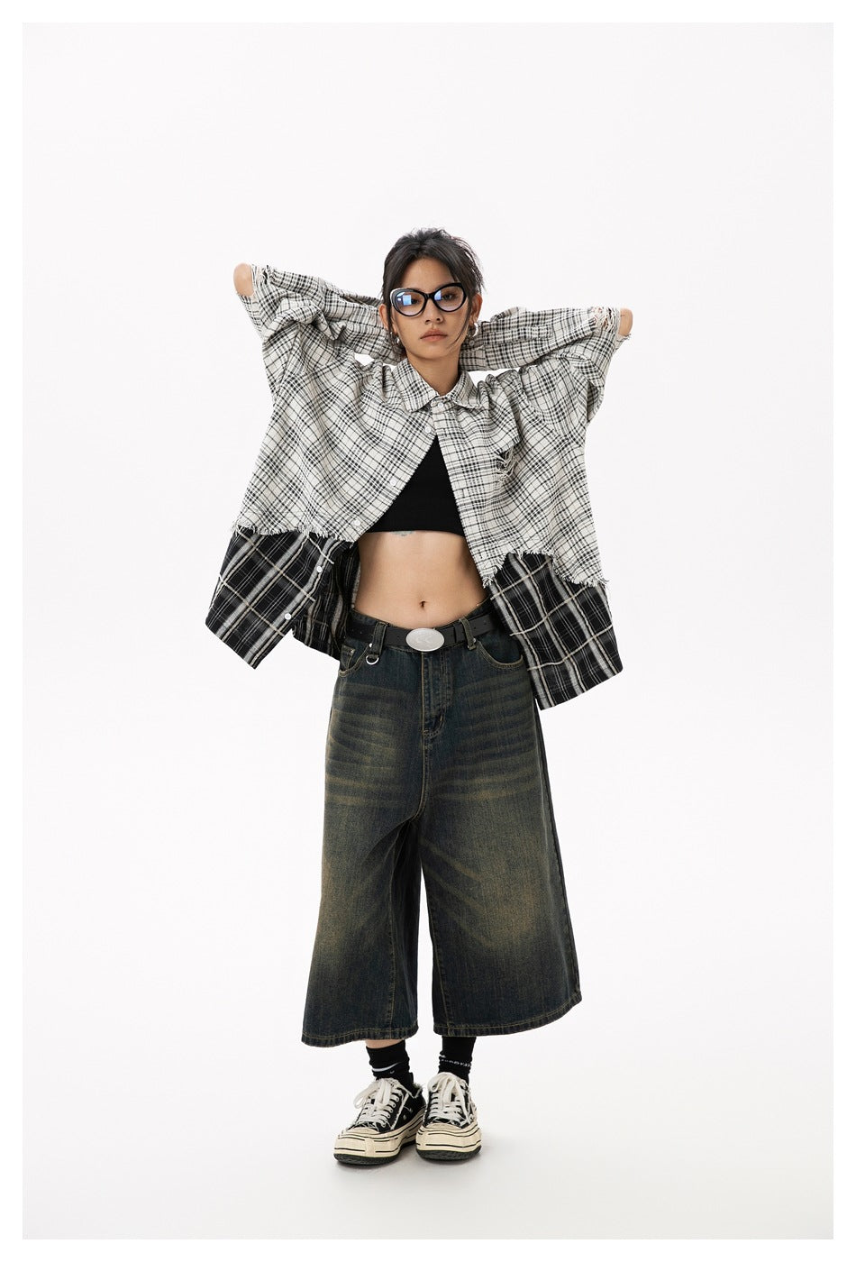 Model with arms raised, showing the layered black-and-white plaid shirt and dark wide-leg cropped jeans.
