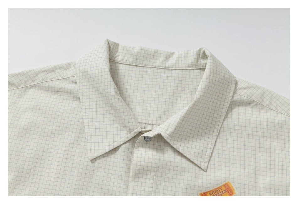 Close-up of the pointed collar and upper front of a cream shirt with a fine blue grid check.