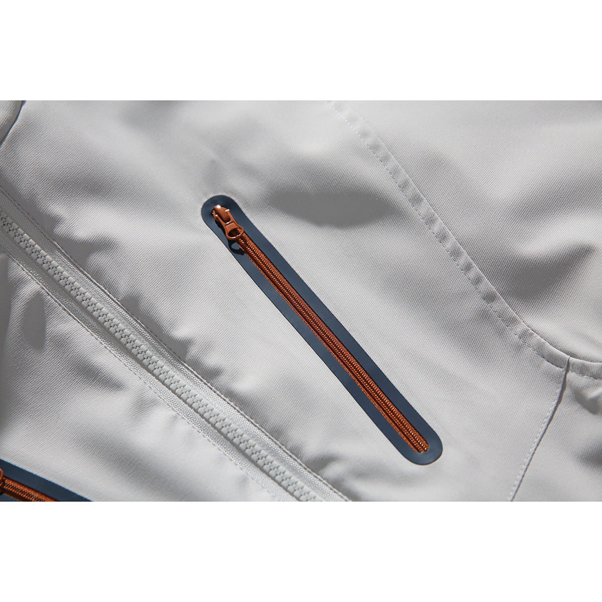 Close-up of an orange zipper with a dark border on light gray jacket fabric, beside the main front zipper.