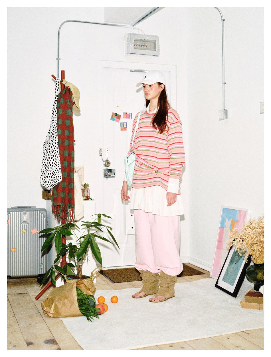 Three-quarter view of model wearing a pink, green and white striped long-sleeve top, white skirt and pink trousers.